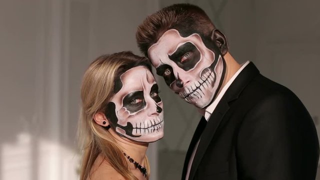 Portrait of a young couple in the Halloween mask. Close-up view of couple of painted halloween holy chracters woman and man. Loving young couple with sugar skull make-up.