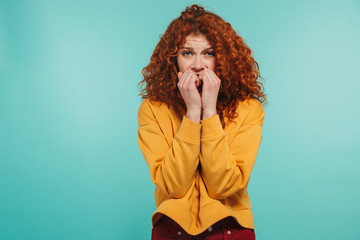 Photo of scared girl 20s with curly ginger hair looking at camera and biting her nails