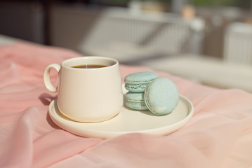 Fototapeta na wymiar French blue macaroon and coffee cup standing on a wooden table with a pink tablecloth white vase with flowers roses and greens.