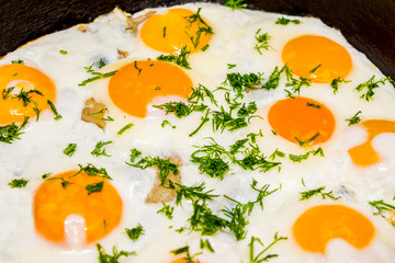 Fried eggs in a frying pan with green dill during cooking_