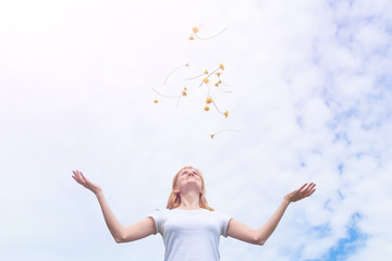 The concept of a happy summer joy. A young girl with blond hair in a white T-shirt stands against the sky. She smiles. Yellow dandelions are thrown up. Freedom, dreaminess.