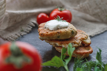 Dietary cheese cakes with sour cream, dill, parsley lie on wood surface, red tomatoes