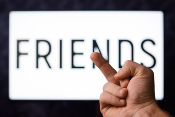Boy having no desire to spend time for his friends shows middle finger to inscription FRIENDS on the screen