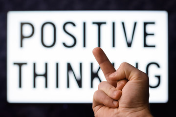 Angry male showing middle finger to a screen with inscription POSITIVE THINKING
