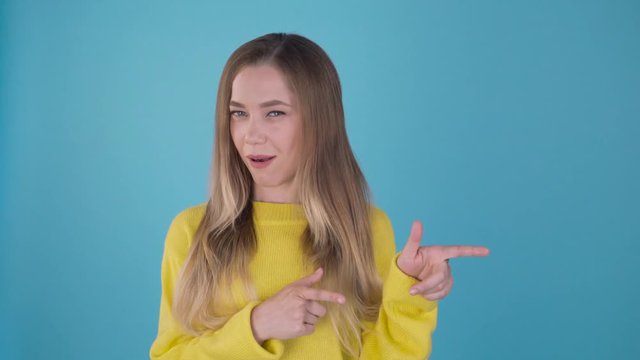 Oh yeah! this and this! Cute funny girl in a yellow sweater shows her fingers in different sides. Isolated blue background. 4K