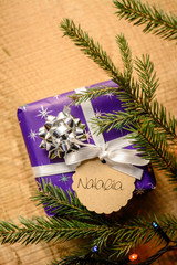 Purpule Christmas gift box near the branch of christmas fir tree on a wooden background