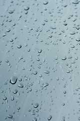 Rain drops on a window glass surface against a dark background of stormy sky.