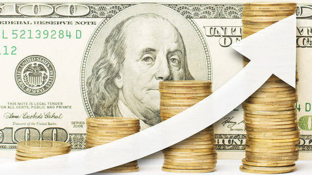 Close Up Photo Of Golden Coins With White Arrow Showing Upward Direction Against A One Hundred US Dollar Bill At The Background