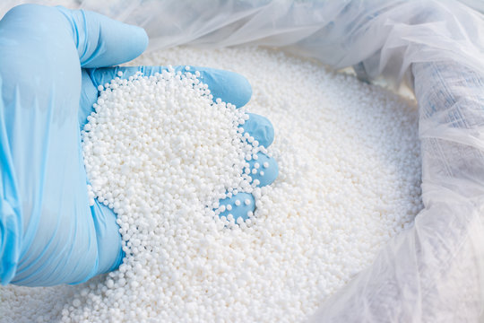 Hand in blue glove holds white fertilizer for plants. Big bag with chemical NPK fertilizer for plants