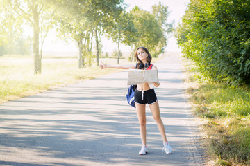 Tired tourist girl tries to hitchhike a car at the country road. Exhausted tourist with heavy bag stops a car to bring herself to the town