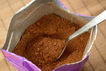 Metal spoon in a big pack of ground coffee against a brown bamboo backdrop