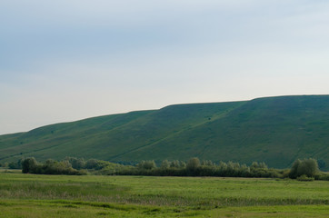 Obraz premium Summer landscape hills and meadows at sunrise with blue sky and green grass