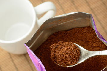 Spoon with some ground coffee against a big pack of coffee near the empty cup. Making coffee in the morning