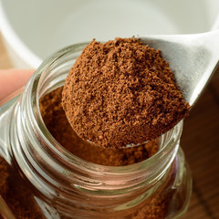 Close up photo of coffee in the spoon over the jar and empty cup.
