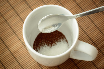 Pouring sugar from a spoon to the cup with coffee.