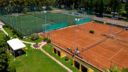 Aerial view perpendicular to two soccer fields at 5 and a red ground tennis court. On board camp benches and umbrellas. The fields are empty because it is summer and hot.