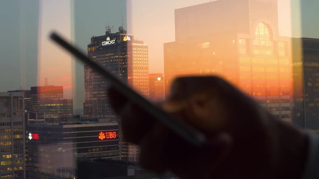 NEW YORK, UNITED STATES OF AMERICA, DECEMBER 2017: CLOSE UP DOF: Scenic shot of corporate skyscrapers illuminated by burnt orange sunset as the woman writes a text message from her office in New York.