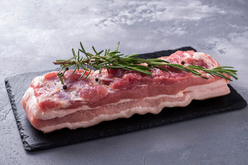 Uncokked pork brisket with salt, pepper and rosemary on a black stone