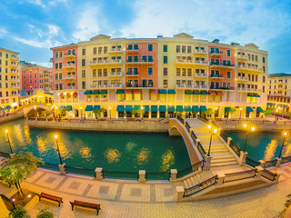 Wide angle view of two Venetian bridges on canals of picturesque district icon of Doha illuminated at night. Panorama of Venice at Qanat Quartier, the Pearl-Qatar, Middle East. Twilight shot.