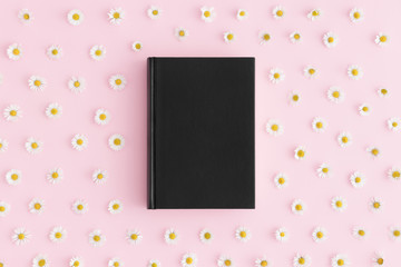 Top view of a black book mockup with daisy decoration on a pink background.