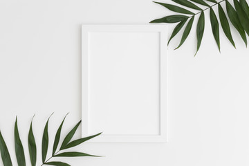 Top view of a white frame mockup with palm leaf decoration. Portrait orientation.