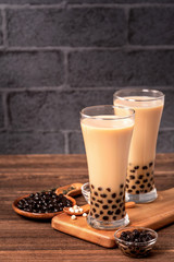 Delicious bubble milk tea with tapioca pearl ball in glass on wooden table and dark gray brick background, popular food and drink in Taiwan, close up