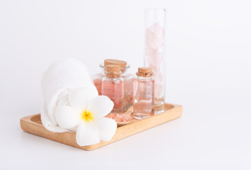 Fototapeta na wymiar Spa and beauty treatment with rose liquid soap,pink Himalayan salt,rose quatz stones,white towel and Plumeria flowera on wooden tray over white background