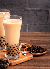 Delicious bubble milk tea with tapioca pearl ball in glass on wooden table and dark gray brick background, popular food and drink in Taiwan, close up