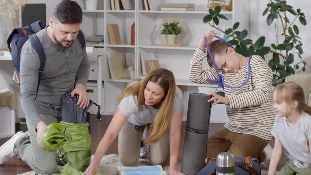 Equipped Caucasian family unpacking stuff for camping while sitting on carpet in their living room