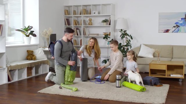 Wide shot of equipped Caucasian family making preparations for camping while sitting on carpet in their living room