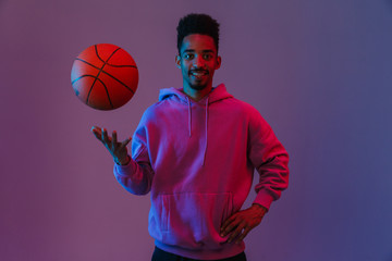 Portrait of masculine african american man in colorful hoodie poising at camera with basketball