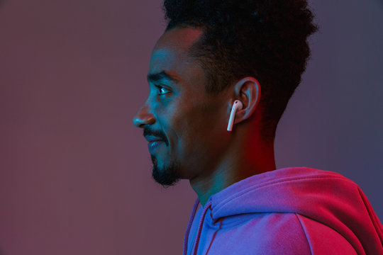 Portrait in profile of positive african american man in colorful hoodie listening to music with earpod