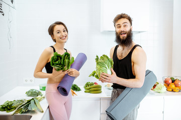 Portrait of a young couple in sportswear standing together with yoga mats and healthy fresh food on...