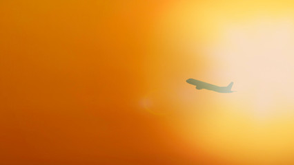 Silhouette of Commercial passenger airplane flying at sunset against golden sky and bright sunlight