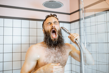 Bearded man feeling shocked while taking a shower with cold water in the bathroom at home
