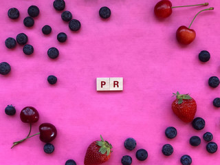Naklejka na ściany i meble PR - public relations - written with letter pieces on pink background covered with berries. Marketing concept. Copy space