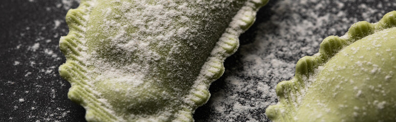 panoramic shot of green raw ravioli with flour on black table