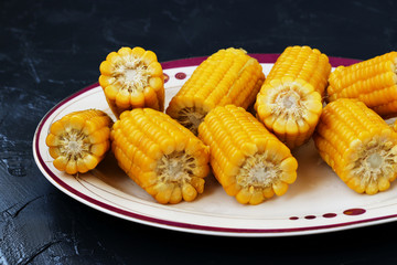 Boiled corn is located on a plate on a dark background