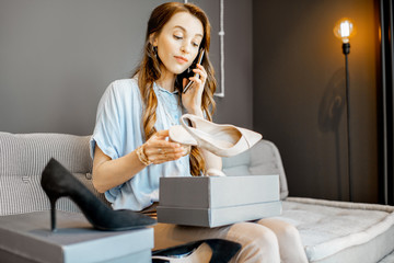 Young woman unpacking parcels with footwear, feeling happy with new online purchases, sitting on the couch at home