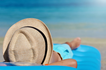 European boy is relaxing at the seashore, he is laying on the inflatable blue mattress, and enjoying his summer holidays.