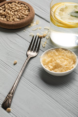 close up view of silver fork, glass of water with lemon and grated cheese on wooden table