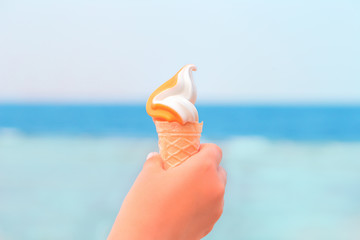 Hand of a child holding an ice cream cone with ice cream against blue sea. Summer heat fun and exotic vacation concept with copy space