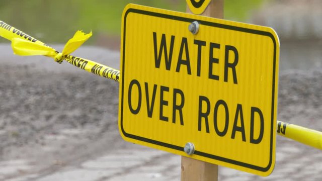 A bright yellow Water Over Road warning sign posted after a flood