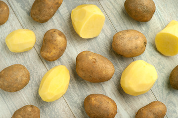 Background of raw and peeled potatoes. Potatoes on a wooden background. View from above. Vegetables in the kitchen. Potatoes peeled and raw for cooking.