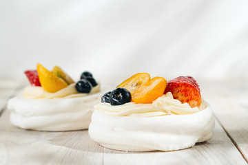 one Pavlova's meringue cake with cream and glazed fruit on white wooden table