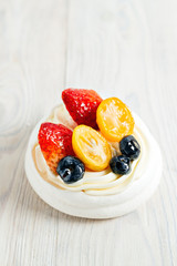 Pavlova's meringue cake with cream and glazed fruit on white wooden table