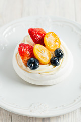 Pavlova's meringue cake with cream and glazed fruit on white plate on wooden table