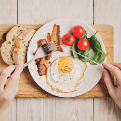 Hands of man in frame. Top view of tasty bacon, one egg and two pieces of bread on the wooden table.