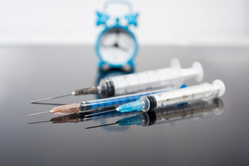 Vaccination time. Vaccine in vial with syringe on clock background. Prevention immunization illness.