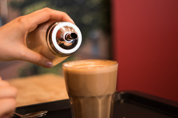 A woman pouring sugar into a milky glass of coffee.